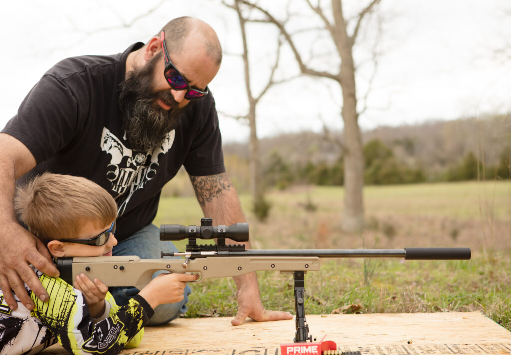 Father teaching son to shoot a suppressed rifle